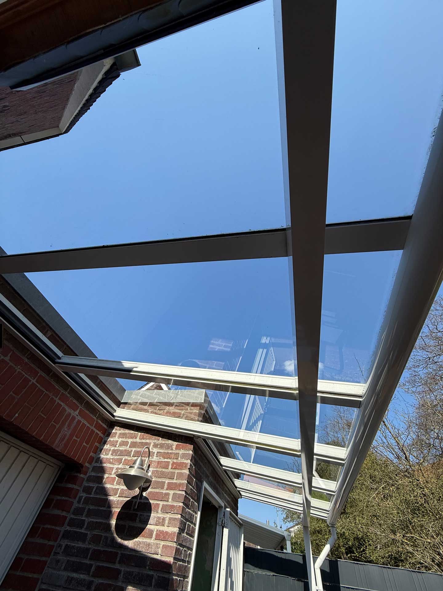 Blick von unten auf ein modernes Glasdach mit klarblauem Himmel darüber