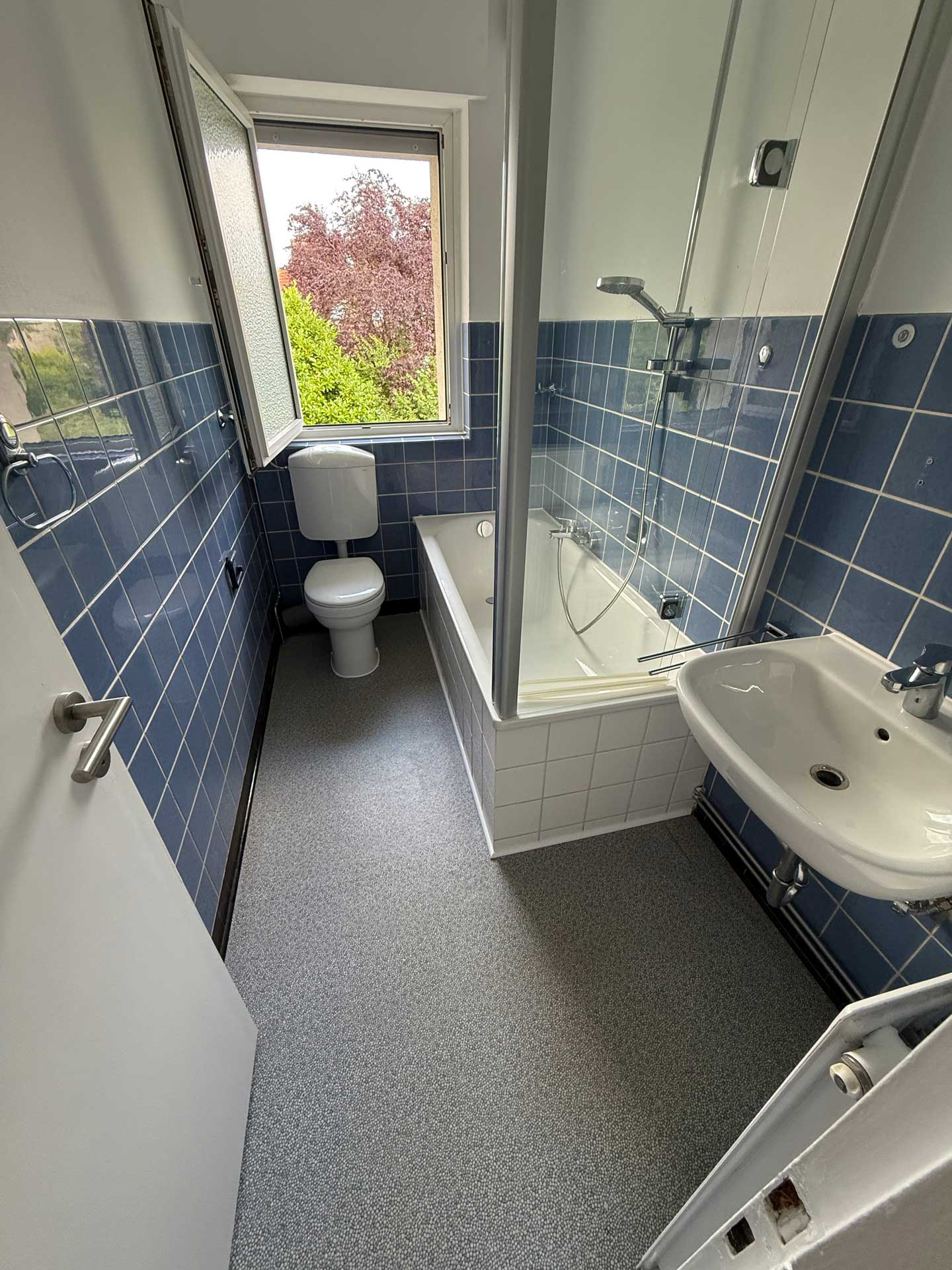Kleines, helles Badezimmer mit blauen Fliesen und einem Fenster zur Natur.