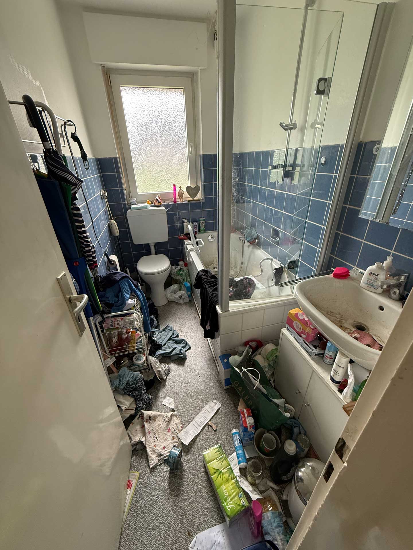 Ein unordentliches Badezimmer mit blauen Fliesen und vielen verstreuten Gegenständen.
