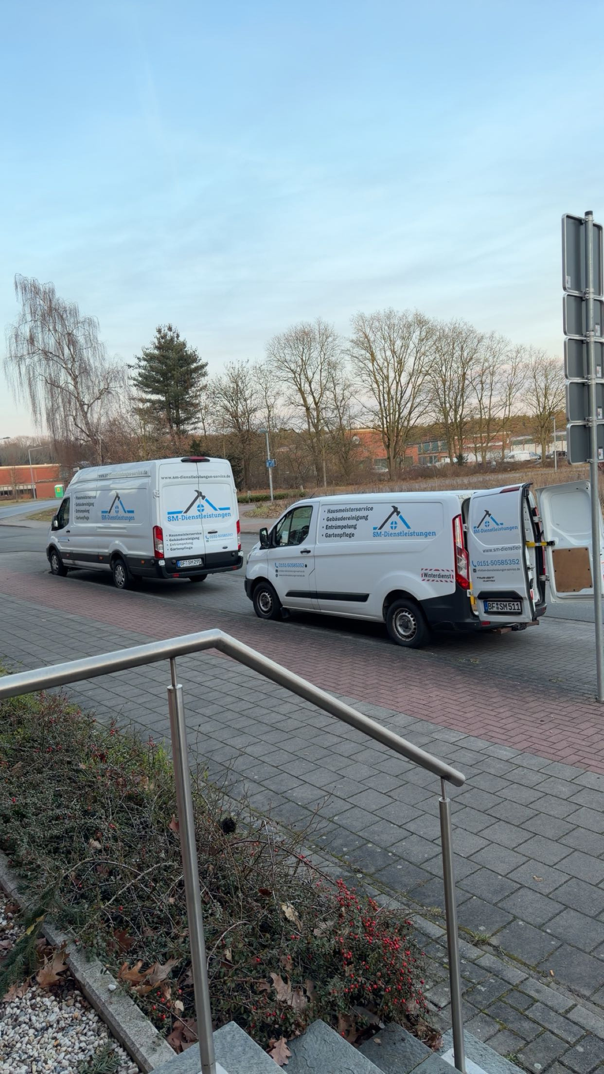 Zwei weiße Lieferwagen mit Firmenlogos stehen nebeneinander auf einer Bordsteinkante